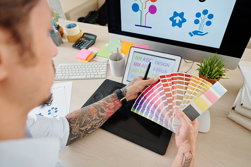 Someone holding a color palette with designs on computer screen. 